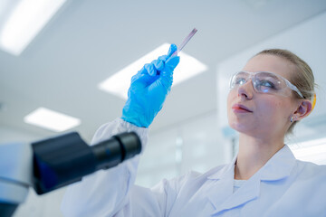 Researcher examines sample under laboratory lighting while wearing protective gear and gloves