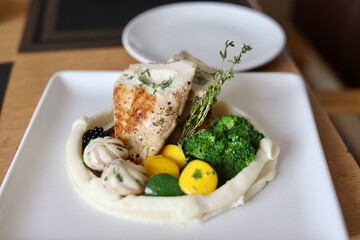Grilled chicken with vegetables on the side served on a fancy white plate in a restaurant or cafe background 