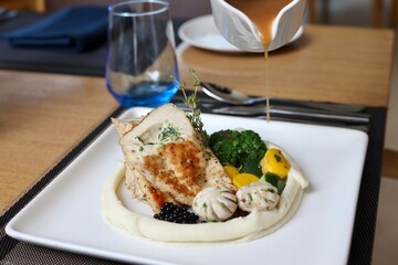 Grilled chicken with vegetables on the side served on a fancy white plate in a restaurant or cafe background 