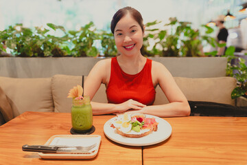 A smiling young woman enjoys a healthy, fresh salmon sandwich for a nutritious meal at Bartels Thailand at True Digital Park in Bangkok