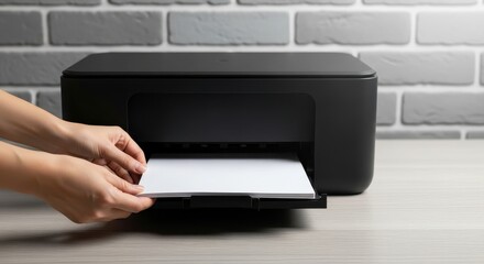 Fototapeta premium A person's hands carefully loading a single blank white sheet into a modern black desktop printer