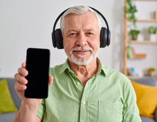 A senior man with headphones learning a new language on a smartphone. A concept of lifelong learning