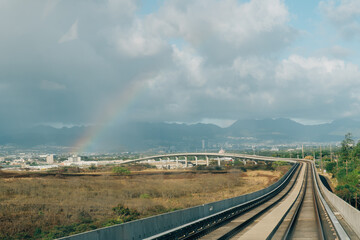 Railway tracks curving towards rainbow with cloudy mountain ridge