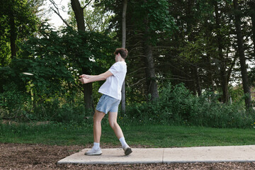 Teenager throws disc off tee box while playing disc golf in forest
