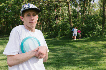 Teen boy holds his disc golf frisbee close while family in background