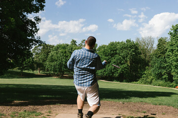 Man throws disc golf frisbee over field towards trees while playing