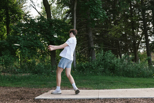 Teenager throws disc off tee box while playing disc golf in forest