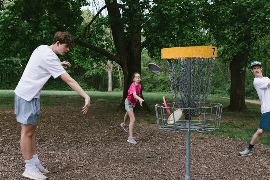 Siblings throw putters into disc golf basket while playing together