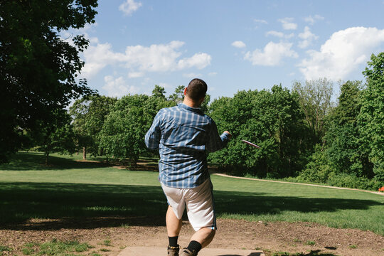 Man throws disc golf frisbee over field towards trees while playing