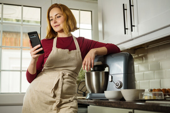 Middle age woman millennial with smartphone cooking in the kitchen