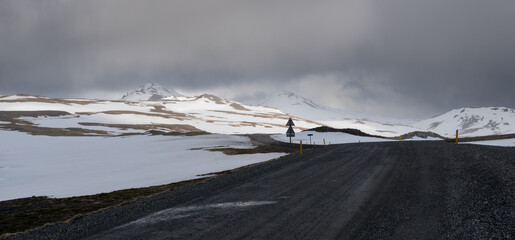 Drive along a rugged mountain road in Iceland under cloudy skies near snow-covered peaks....
