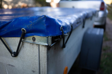 Small , covered luggage trailer focus on the blue plastic cover, space for text.