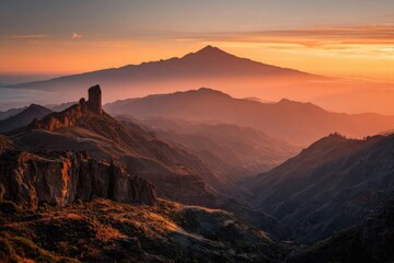 Naklejka premium Majestic mountain vista at sunrise. Golden hues paint a valley, with a volcanic peak in the distance. Rocky terrain and a solitary rock formation are foreground elements