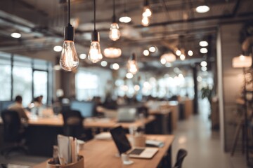 A blurry, warm-toned open office with wood desks, suspended filament bulbs, and workers in the background. Focus on desk nearest camera