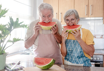 Happy senior caucasian couple in home kitchen ready to eat a red watermelon slice - hydration,...