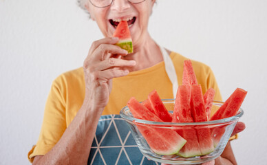 Cheerful elderly woman holding a bowl of freshly watermelon's slices isolated on white background -...