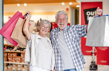 A happy senior couple looking at the camera while shopping in a store, taking advantage of sales and offers. A concept of sales and consumerism.