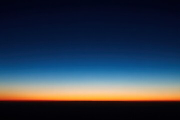 A vibrant sunset horizon seen from high above.  Deep blue and dark navy sky fades to an orange-red band at the horizon