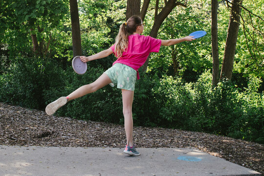 Girl throws a driver disc while playing disc golf in nature