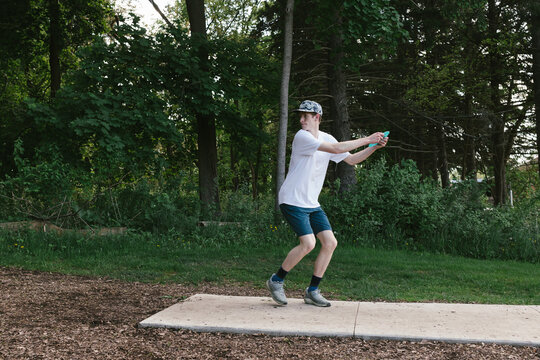 Boy prepares to throw disc while playing disc golf in woods