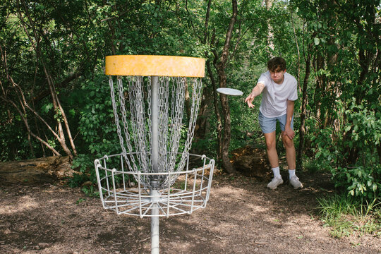 Teenage boy putts while playing disc golf outside in forest