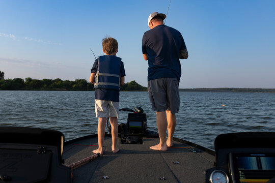Father and son fishing together on boat facing lake horizon