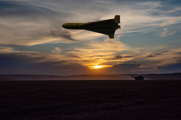 A military drone flies over a field in the rays of the setting sun.