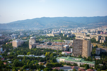 Obraz premium A wide panoramic view of Tbilisi, Georgia, featuring residential apartment blocks, modern buildings, and the scenic backdrop of the Caucasus mountains. The urban and natural blend of Georgian people