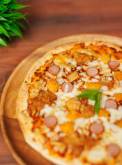 Close up tasty chicken sausage crispy thin pizza baked on wooden plate, delicious melting mozzarella cheese on wooden board, homemade cooking ingredients lying on dark background, food advertisement.