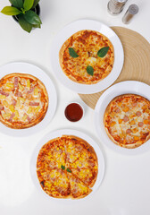 Top view of composition different delicious tasty crispy pizza, flatbread baked on white dish with decoration on table, homemade cooking ingredients lying on light background, food advertisement