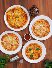 Top view of composition different delicious tasty crispy pizza, flatbread baked on white dish with decoration on wooden table, homemade cooking ingredients lying on dark background, food advertisement