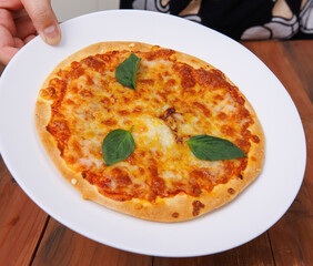 Tasty cheese crispy pizza flatbread baked on white dish plate, delicious melting mozzarella cheese on wooden table board, homemade cooking ingredients lying on dark background, food advertisement.
