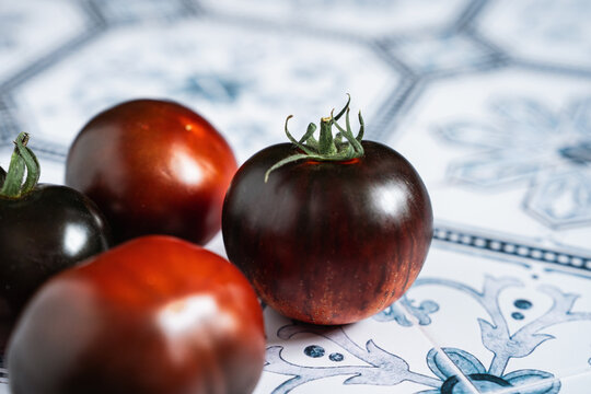 close-up of Ripe red and black beauty tomatoes on white plate with blue rim. Tiled kitchen table. Cooking with copy space. Tomatocore