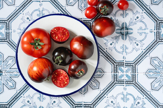 Ripe red and black beauty tomatoes on white plate with blue rim. Tiled kitchen table. Cooking with copy space. Tomatocore