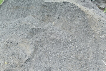 Pile of fine gray sand or aggregate used for construction, captured in natural light, showing granular texture and earthy tones, ideal for industrial or material background use.