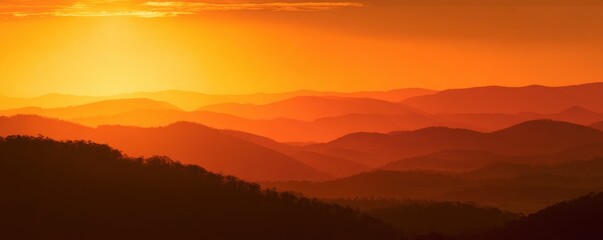 Obraz premium Golden sunset over a range of mountains. Silhouette of forested hills bathed in warm, orange light