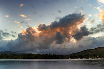 Billowing clouds above a lake, highlighted with the colours of a setting sun. Billowing clouds with warm colours of a setting sun above Lake Windermere