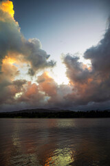 Fototapeta premium Billowing clouds above a lake, highlighted with the colours of a setting sun. Billowing clouds with warm colours of a setting sun above Lake Windermere