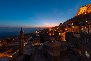 Mardin cityscape with roof of a Turkish hammam and minarets in Mardin old town at sunset,...