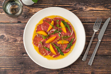 Thinly sliced beef carpaccio with orange segments and arugula leaves