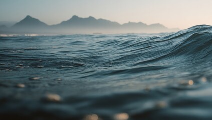 Close-up view of ocean waves gently lapping the shore, with distant misty mountains in the background
