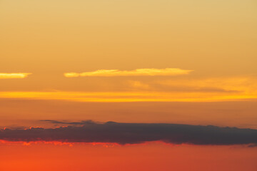 Obraz premium Vibrant colorful sunset sky with a warm orange and red gradient, featuring layers of dark and glowing clouds.