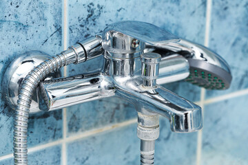 Obraz premium Bathroom chrome faucet with shower hose. Water tap closeup on blue tiles background. Sanitary installation in home interior. Plumbing equipment detail. Household bathroom hygiene element.