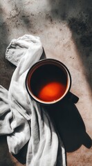 A cup of dark liquid sits on a textured surface with a white cloth, under bright sunlight casting strong shadows, creating a minimalist aesthetic