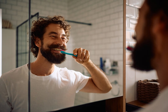 Reflection in mirror of happy man brushing his teeth.