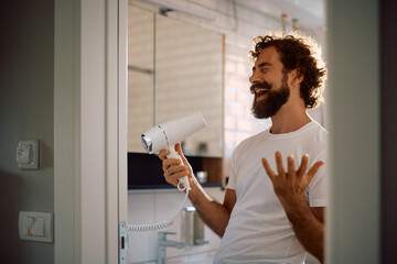Happy man having fun while using hair dryer in bathroom.