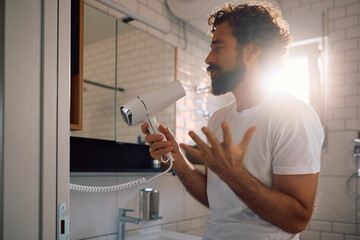 Mature man singing into hair dryer and having fun in bathroom.