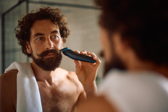 Mature man using electric razor while shaving in bathroom.