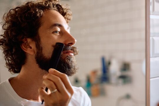 Smiling man using comb while styling his mustache in bathroom.