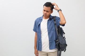 Young Asian student man wearing casual clothes and backpack, having doubt and confused facial...